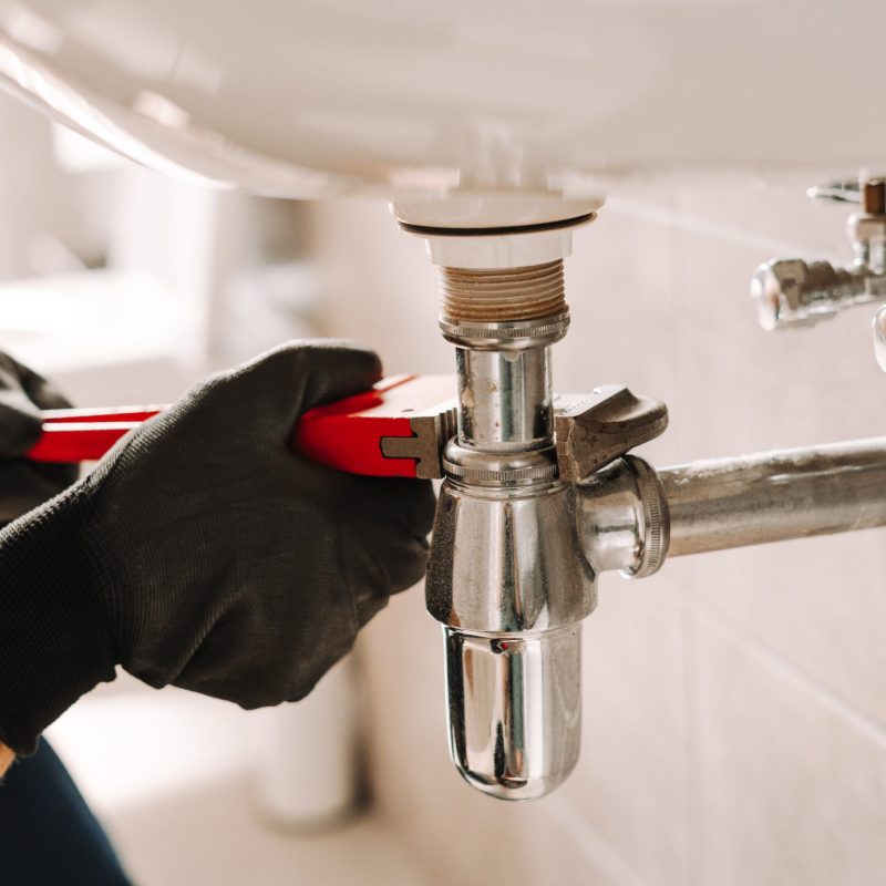 Plumber in black gloves fixes a sink pipe with a wrench in a bathroom, showcasing precision and craftsmanship